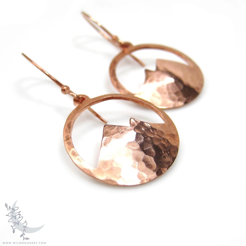 May include: A pair of copper earrings with a hammered texture. Each earring features a circular design with a mountain silhouette cut out.