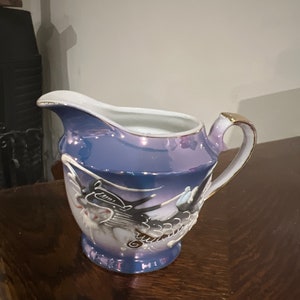 Peut inclure: Un pot à crème en porcelaine bleu et blanc avec un bord doré et un motif de dragon. Le pot à crème a une anse et un bec.