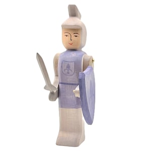 May include: A wooden toy knight with a purple tunic, a sword, and a shield with a fleur-de-lis design. The knight has a painted face with a smile.