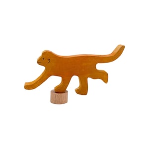 May include: A wooden toy monkey with a brown finish, standing on a wooden base. The monkey has a simple, hand-painted face.