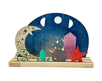 May include: A wooden play set with a blue crescent moon, stars, and crystals. The set is made of natural wood and is painted in a variety of colors. The set is perfect for imaginative play and can be used to create a variety of scenes.
