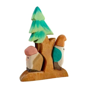 May include: Wooden toy set featuring two figures with painted faces and a green tree. The figures are standing next to a brown tree trunk with a green tree on top. The figures are wearing hats and have painted details.