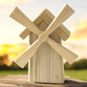 Puede incluir: Un juguete de molino de viento de madera con un acabado blanqueado y cuatro aspas. El molino de viento está sentado en una mesa de madera contra un fondo borroso de un cielo de puesta de sol.