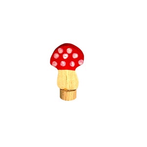 May include: A red and white wooden mushroom toy with white dots on the top. The mushroom is on a wooden base.
