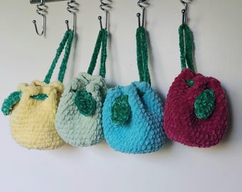 Pode incluir: Quatro pequenas bolsas de cordão de crochê penduradas em ganchos. As bolsas são de cor amarela, verde, azul e bordô. Cada bolsa tem uma folha de feltro verde.