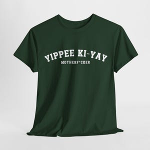 Puede incluir: Camiseta verde oscuro con la frase "Yippee Ki-Yay Motherf*cker" en letras blancas, en negrita y mayúsculas. La camiseta es de cuello redondo y parece estar hecha de un material suave.