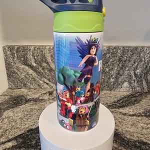 May include: A stainless steel water bottle with a blue and green lid. The bottle features a colorful graphic of characters from a video game. The characters are set against a cityscape background. The bottle is sitting on a white pedestal.