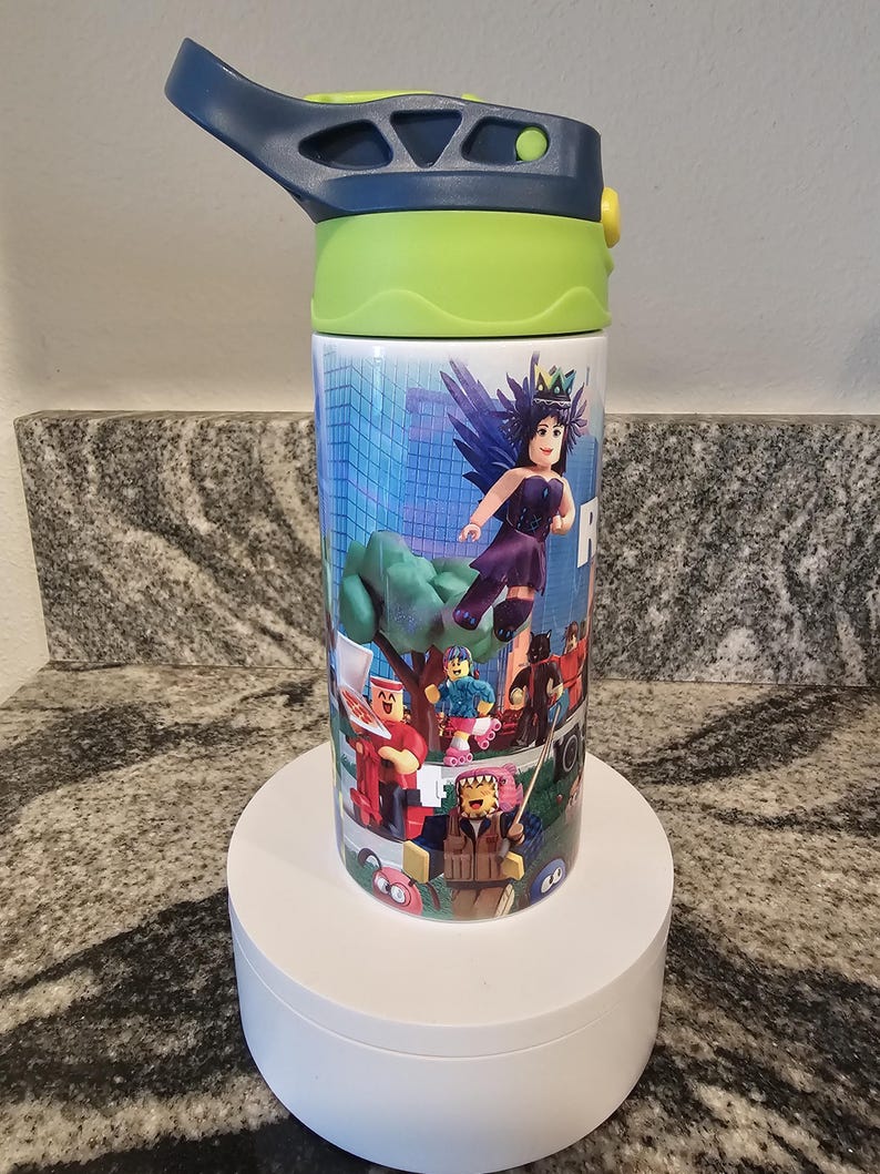 May include: A stainless steel water bottle with a blue and green lid. The bottle features a colorful graphic of characters from a video game. The characters are set against a cityscape background. The bottle is sitting on a white pedestal.