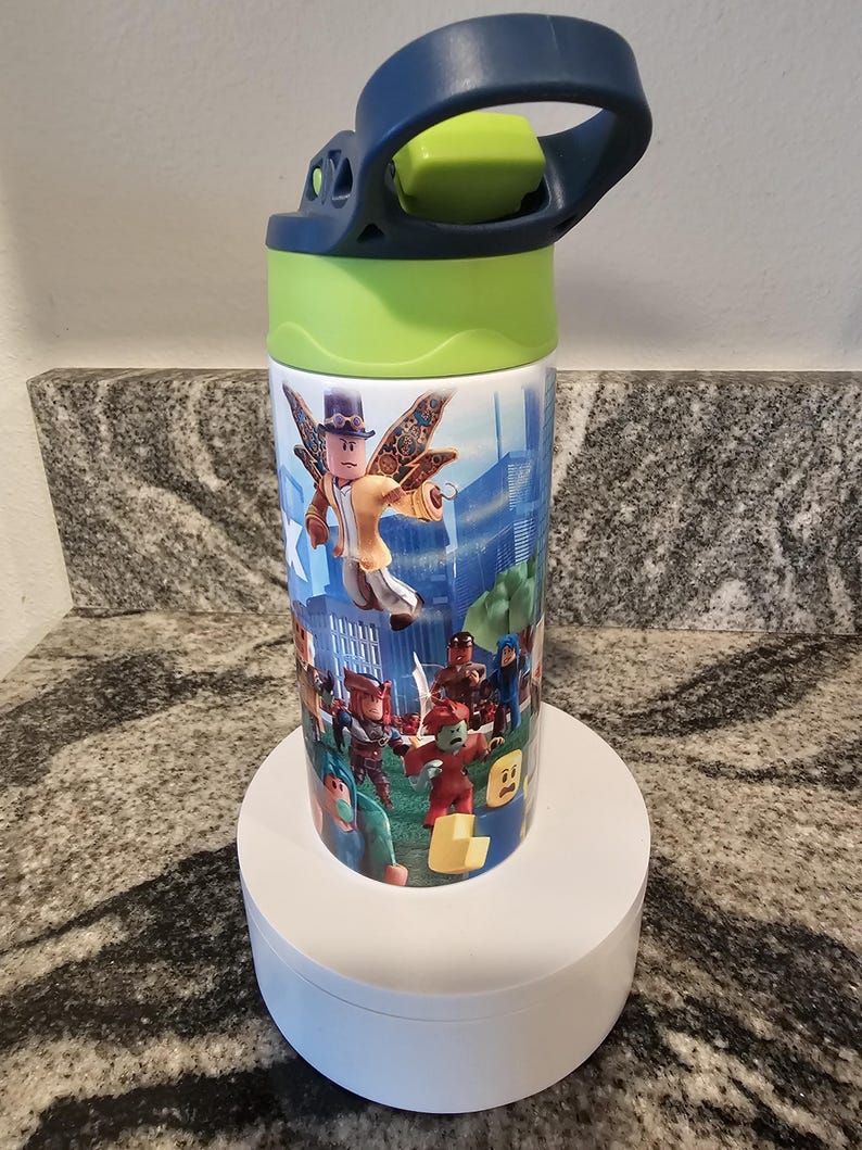 May include: A cylindrical water bottle featuring a colorful design with characters from a popular video game. The bottle has a blue handle and a green lid. The design includes various characters in a city and outdoor setting.