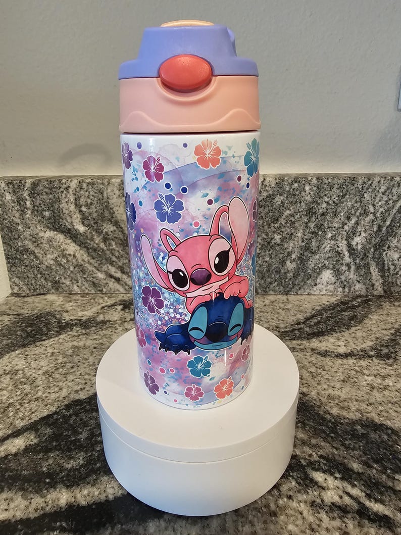 May include: A water bottle featuring a cartoon design of Stitch and Angel from Lilo & Stitch. The bottle has a pink, purple, and blue color scheme with a floral pattern. The lid is pink and purple.