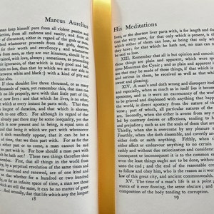 May include: A page from a book titled "Meditations" by Marcus Aurelius. The text discusses the importance of living in the present moment and not dwelling on the past or future. The book is bound in yellow and has a worn, aged appearance.