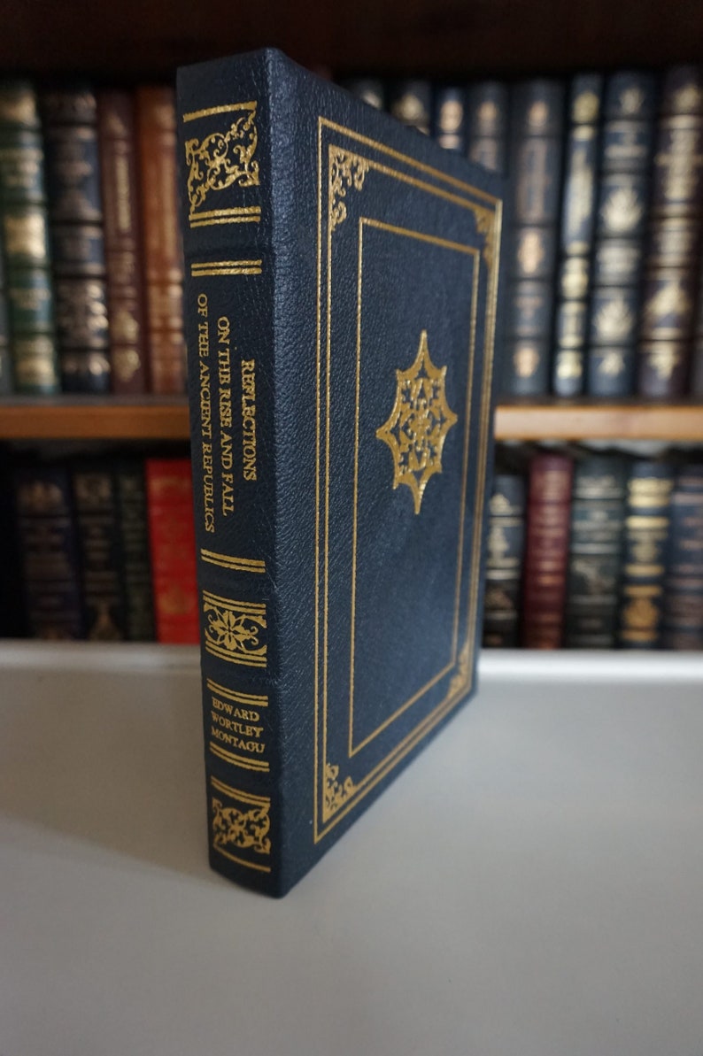 Puede incluir: Un libro de tapa dura azul marino con letras doradas y detalles decorativos. El t&iacute;tulo es "Reflexiones sobre el auge y la ca&iacute;da de las antiguas rep&uacute;blicas" de Edward Wortley Montagu.