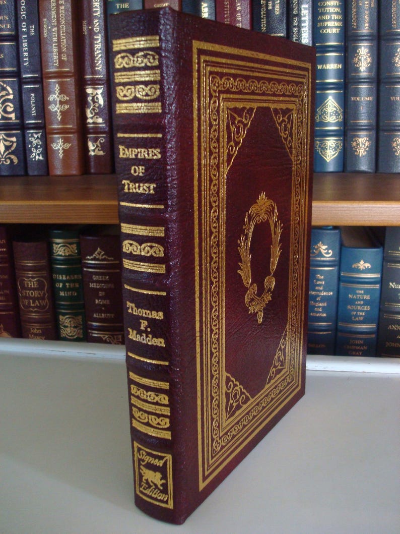 May include: A burgundy leather-bound book with gold accents and the title "Empires of Trust" by Thomas F. Madden. The book is a signed edition.