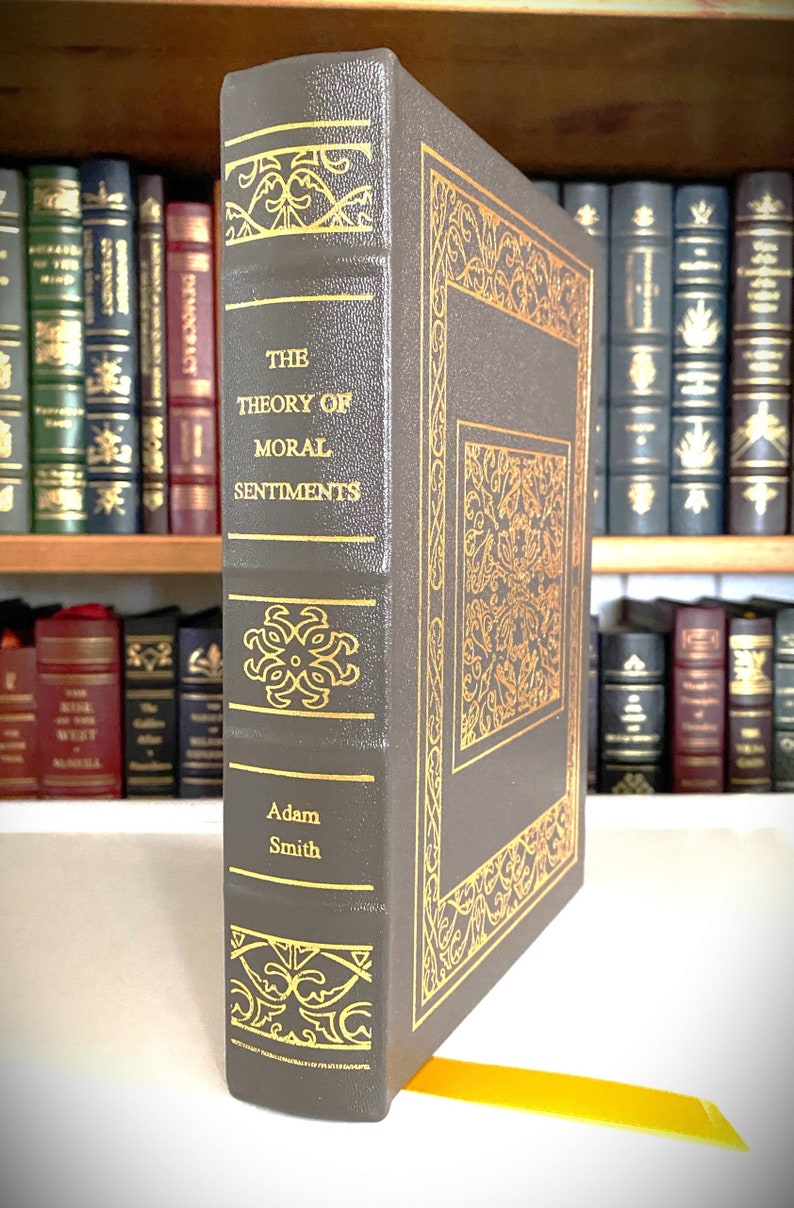 May include: A dark gray hardcover book with gold accents and the title "The Theory of Moral Sentiments" by Adam Smith.