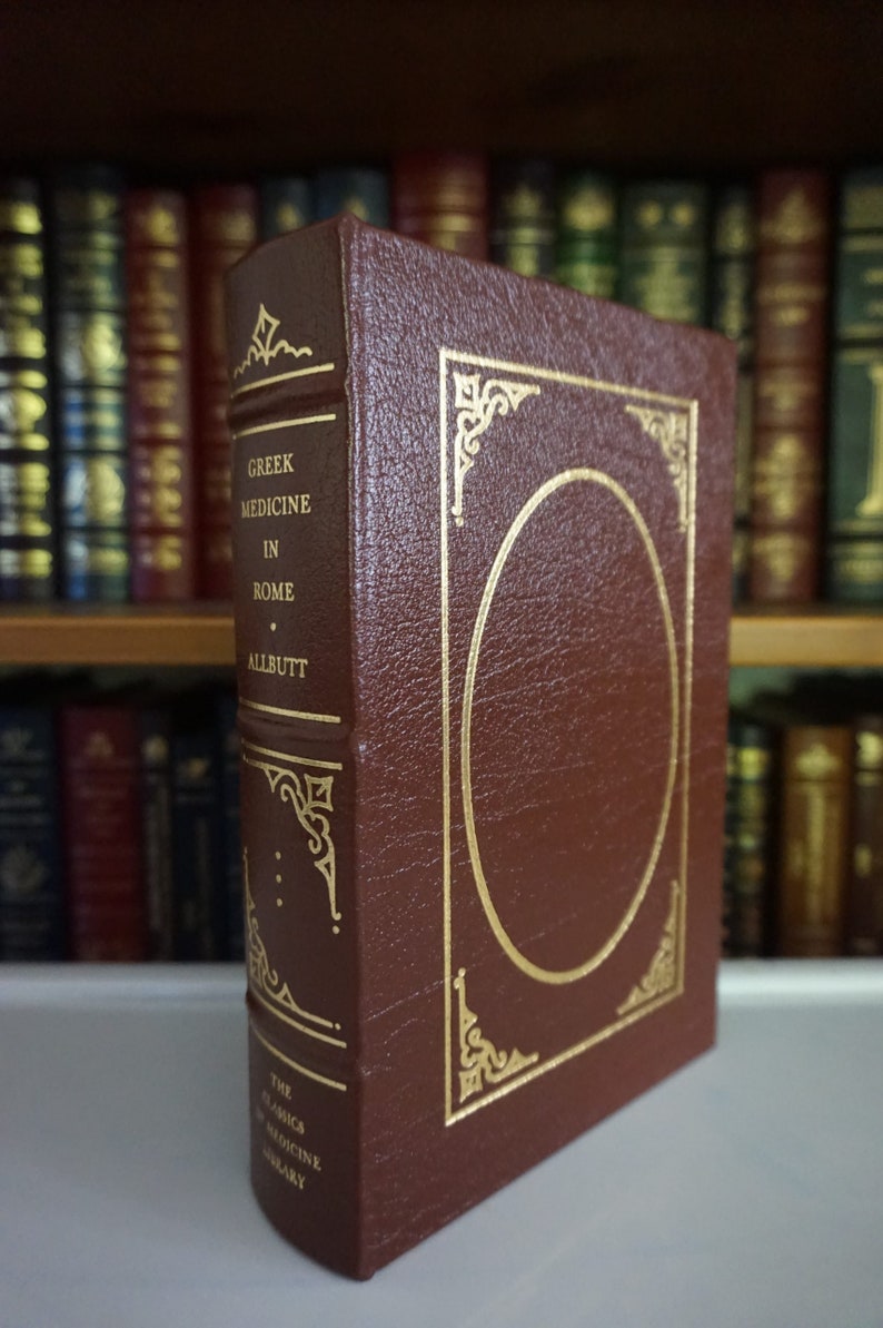 Puede incluir: Un libro encuadernado en cuero marr&oacute;n con detalles dorados y el t&iacute;tulo "Greek Medicine in Rome" de T.C. Allbutt. El libro forma parte de "The Classics of Medicine Library".