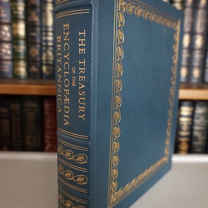 May include: A dark blue leather-bound book with gold lettering on the spine. The title is "The Treasury of the Encyclopedia Britannica".