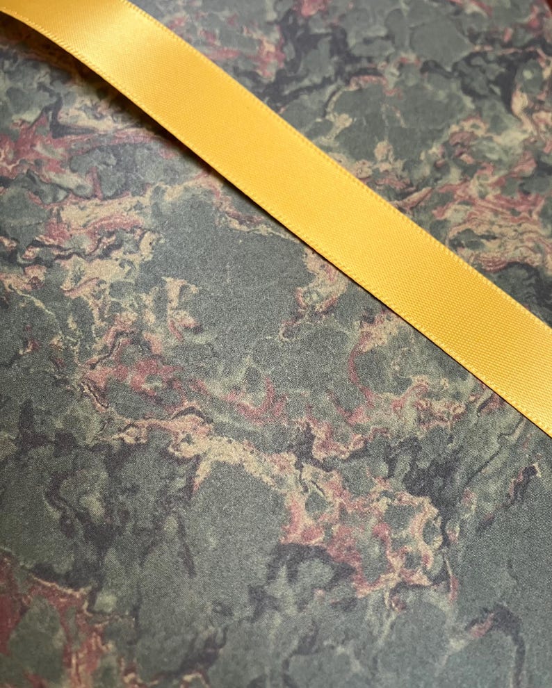 May include: A close-up of a yellow satin ribbon on a green, brown, and pink marbled background.