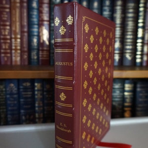 Puede incluir: Un libro encuadernado en cuero burdeos con letras doradas y un dise&ntilde;o estampado en dorado. El t&iacute;tulo del libro es "Augustus" y el autor es "E.S. Shuckburgh".