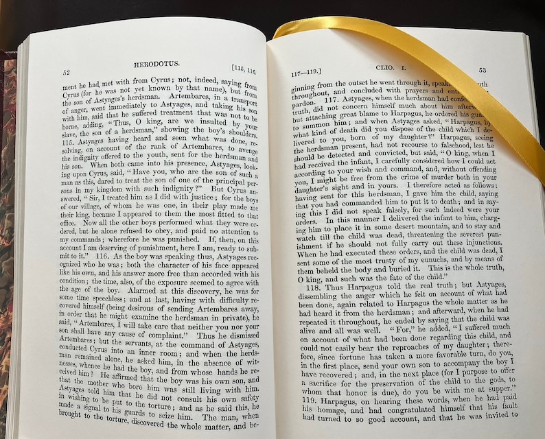 May include: A close-up of a page from a book titled "Herodotus" with text about the story of Cyrus, the son of Astyages, and his treatment by the son of a herdsman. The text is in black and white.