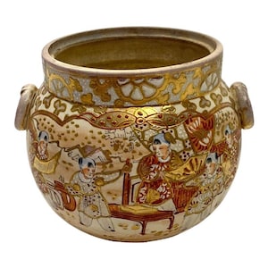 Puede incluir: Una olla redonda de cerámica antigua con dos asas. La olla presenta una escena detallada pintada a mano de figuras con vestimenta tradicional, con detalles dorados y rojos. El borde y las asas también están decorados con oro.