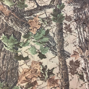 May include: Camouflage fabric with a pattern of brown tree trunks, green and brown leaves, and a beige background.