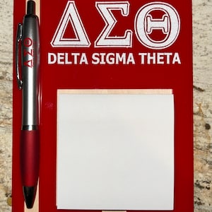 May include: A red notepad with a silver and red pen. The notepad features the Greek letters Delta, Sigma, and Theta in white, along with the words DELTA SIGMA THETA. A pad of white sticky notes is attached.