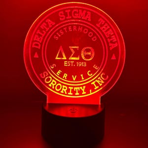 Pode incluir: Uma luz noturna de acr&iacute;lico vermelha e amarela com o texto "Delta Sigma Theta Sorority Inc. Sisterhood Service Est. 1913" e as letras gregas "&Delta;&Sigma;&Theta;" em um c&iacute;rculo.