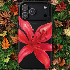 A black phone case featuring a large red tiger lily rests on a lush green mossy surface.