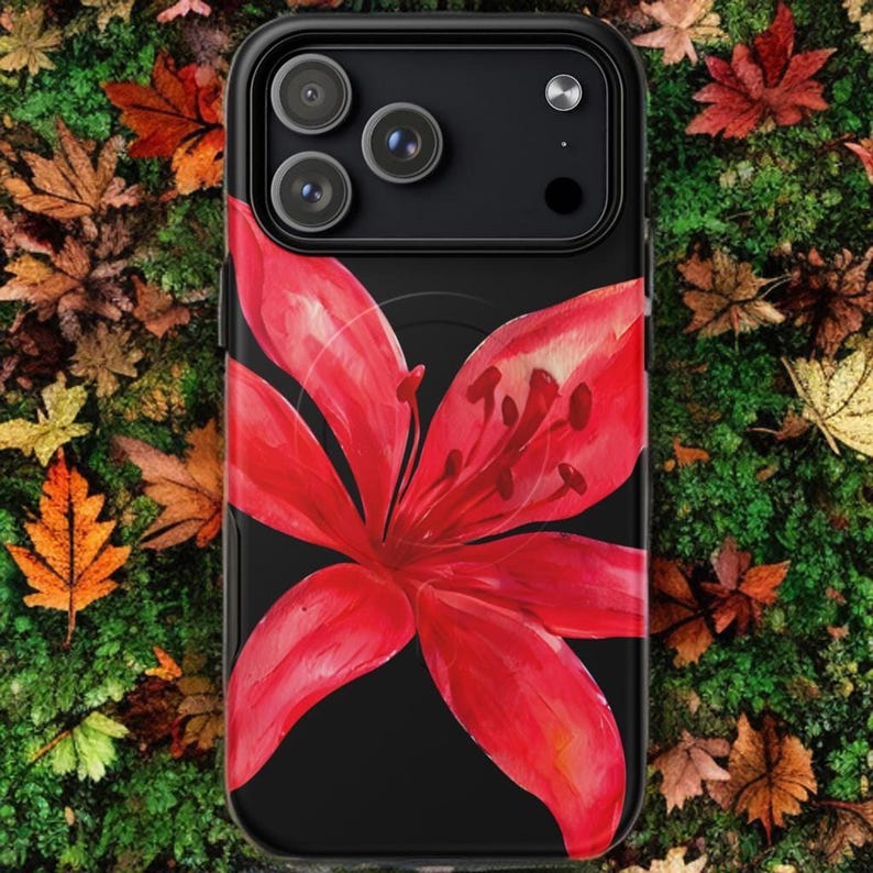 A black phone case featuring a large red tiger lily rests on a lush green mossy surface.