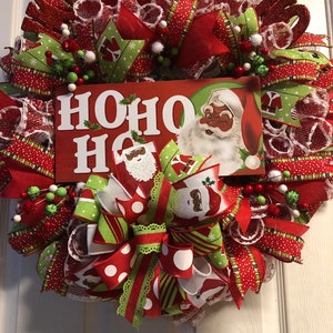 Puede incluir: Una corona de Navidad con cinta roja, verde y blanca, un letrero grande de "HO HO HO" y una imagen vintage de Santa Claus.