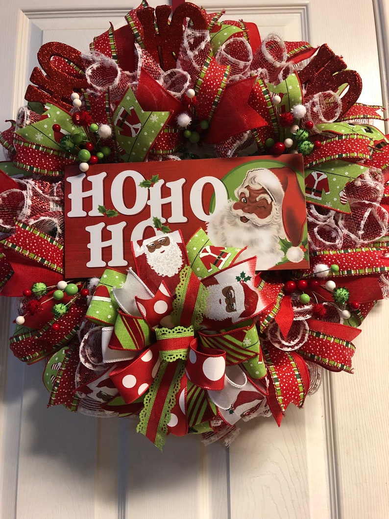 Puede incluir: Una corona de Navidad con cinta roja, verde y blanca, un letrero grande de "HO HO HO" y una imagen vintage de Santa Claus.