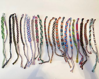 Può includere: Una collezione di 20 braccialetti dell'amicizia colorati con vari motivi e design. I braccialetti sono realizzati con filo da ricamo colorato e hanno nappe alle estremità.