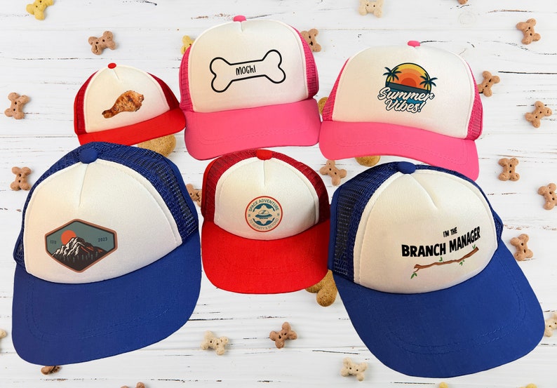 Puede incluir: Cinco gorras de camionero diferentes con dise&ntilde;os variados. Las gorras son blancas con una parte trasera de malla y tienen viseras de diferentes colores. Los dise&ntilde;os incluyen una cordillera monta&ntilde;osa, un hueso con la palabra "Mochi" en &eacute;l, una palmera con las palabras "Summer Vibes", un barco con las palabras "Wild Adventures" y una rama con las palabras "Soy el gerente de la sucursal".
