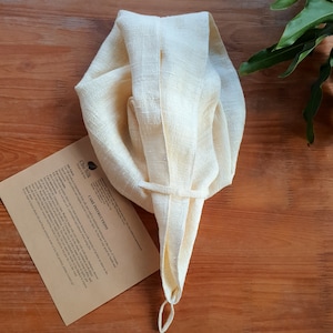 Puede incluir: Una bolsa de tela de seda natural, reutilizable, con cord&oacute;n de ajuste, de color crema. La bolsa est&aacute; doblada y atada con una cuerda. La bolsa est&aacute; sobre una superficie de madera con un trozo de papel con instrucciones de cuidado impresas.