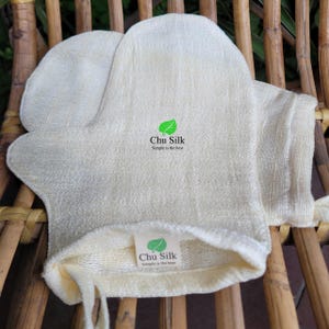 May include: A pair of beige exfoliating gloves with a green logo that says "Chu Silk Simple is the best".