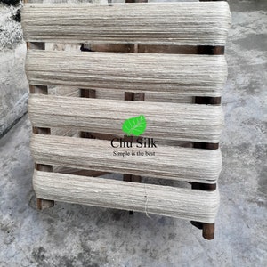 May include: A wooden yarn swift with tightly wound, off-white yarn. The swift has a rectangular frame with horizontal wooden bars and vertical supports. The text "Chu Silk Simple is the best" is visible on the bottom right.