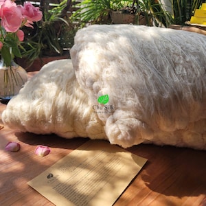 May include: A close-up of a large pile of white cotton fiber. The cotton is soft and fluffy, and it is arranged in a loose, irregular shape. The cotton is labeled "Chu Silk" and the text "Simple is the best" is printed below the logo.