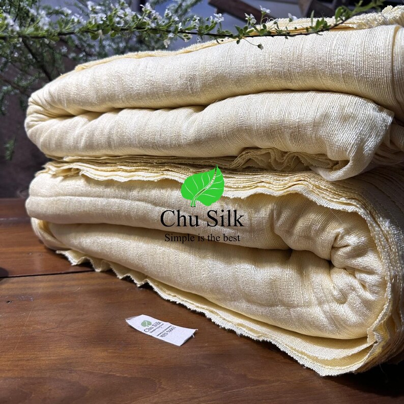 May include: A stack of folded, light yellow fabric. The fabric has a textured appearance and is neatly arranged. The image includes a logo that says "Chu Silk" and "Simple is the best".