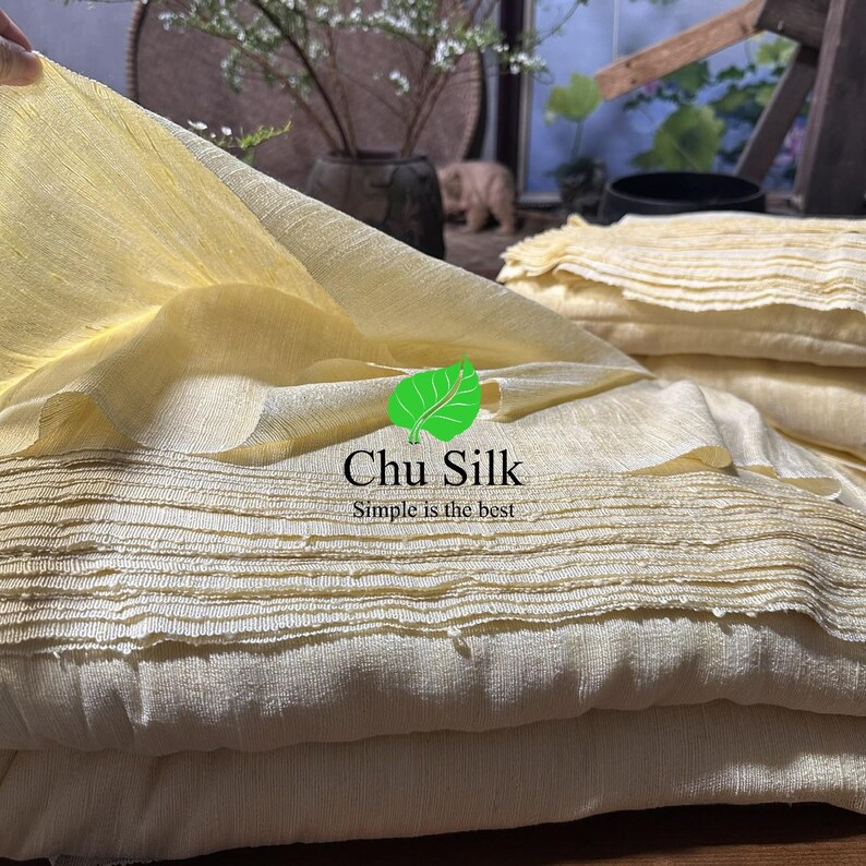 May include: Close-up of folded, light yellow silk fabric. The fabric has a textured, pleated appearance. The image includes the text "Chu Silk" and "Simple is the best".
