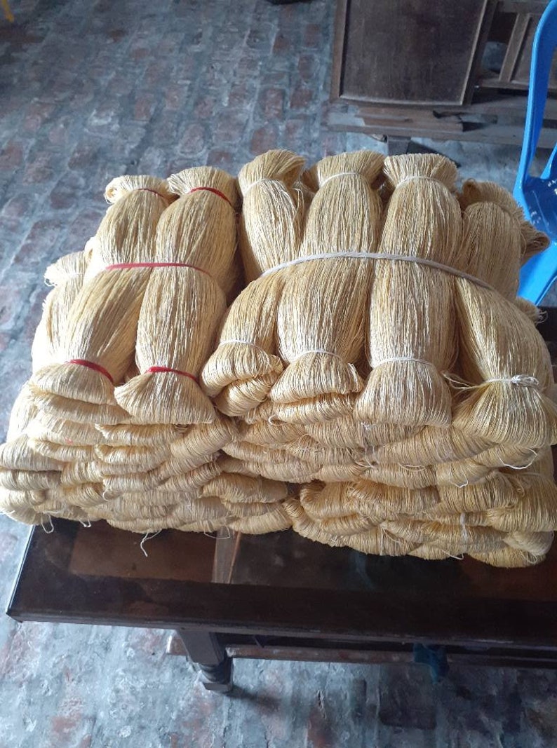 May include: A stack of bundles of golden-colored fiber, tightly bound with red and white bands. The bundles are stacked on a dark wooden table, suggesting a craft or textile material.