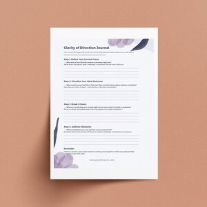 Op de afbeelding: Een printbaar werkblad met de titel "Duidelijkheid van richting Journal" met een paars en zwart aquarelontwerp. Het werkblad omvat vier stappen om je te helpen je huidige focus te defini&euml;ren, je ideale resultaat te visualiseren, het te verdelen en obstakels aan te pakken.