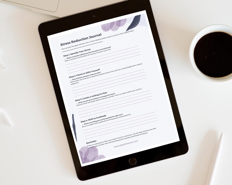 Op de afbeelding: Een digitale tablet met een afdrukbaar stressreductie-dagboek met stappen om stress te identificeren, bij jezelf na te gaan, een loslaatplan te maken en je te richten op dankbaarheid. Het dagboek ligt op een wit oppervlak met een kopje koffie en een witte pen.