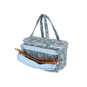 May include: A blue floral tote bag with a zipper closure and a padded interior. The bag is designed for carrying knitting needles and yarn. The bag has two handles and a zippered pocket on the front.