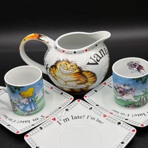 Könnte beinhalten: Eine weiße Keramik-Tasse mit schwarzem Henkel und dem Text "But First, Coffee" in schwarzer, handschriftlicher Schrift. Die Tasse steht auf einer weißen Oberfläche.