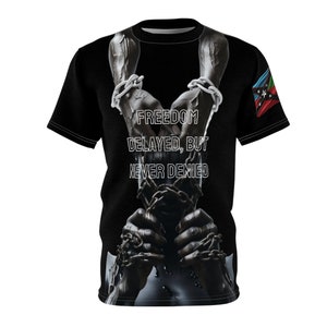 May include: Black t-shirt with a graphic of hands in chains and the text "FREEDOM DELAYED, BUT NEVER DENIED". A flag with red, blue, and green colours is on the right sleeve.