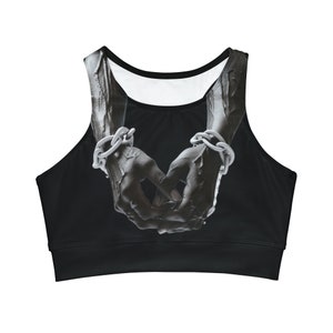 May include: Black sports bra with a grayscale image of two hands clasped, bound by a silver chain. The bra has a scoop neck and a solid black band at the bottom. The interior lining is white.