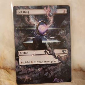 Könnte beinhalten: Eine Sammelkarte mit dem Titel Sol Ring, die eine dunkle, kosmische Illustration eines leuchtenden Rings zeigt, der über einem Steinsockel schwebt. Der Kartentext enthält Artifact, die Zahl 1 und den Text: Add 2 to your mana pool.