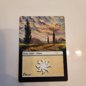 May include: A rectangular trading card titled Basic Land - Plains. The top section features a landscape painting of a field with tall cypress trees under a sunset sky. The bottom section is cream-colored with a white sun symbol and the text Row.