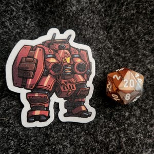 May include: A die-cut sticker featuring a red and orange armored mech robot with thick plating and mechanical details, positioned next to a twenty-sided polyhedral die with brown and white marbled coloring and white numerical markings.