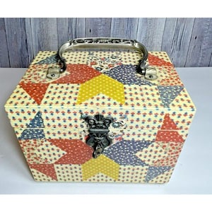 May include: A vintage hexagonal box with a patchwork design. The box features a silver handle and clasp. The patchwork includes red, yellow, and blue patterns on a cream background. The box is likely used for storage or display.